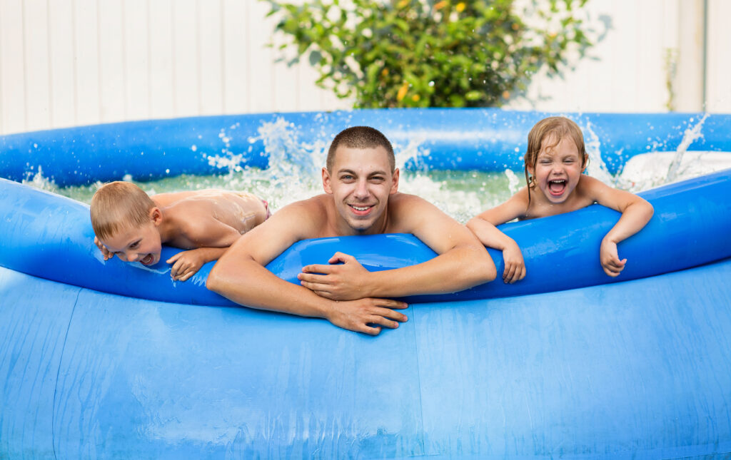Rodzina kąpie się w basenie ogrodowym, który wybrali dla siebie po zastanowieniu czy wolą basen stelażowy czy rozporowy